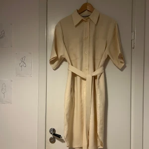 Beige skjortklänning från & Other Stories - Säljer en stilren beige skjortklänning från & Other Stories. Klänningen har korta ärmar, knappar framtill och ett knytskärp i midjan för en snygg passform! Inköpt för ca 899 kr. 