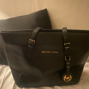 Svart axelväska från Michael Kors - Säljer den billigt pga att texten har gått bort lite men det går att måla över med guldfärg , och att det finns ett jätte litet hål i tyget på botten men de går att sy ihop snabbt, och de är inget som syns utanpå och knappt innanför. Lite knögglig då det är tomt i väskan, annars ser den ut som vanligt med saker i den.