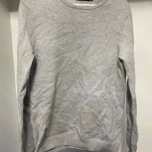 Grå tröja från S.C.W. - Säljer en stilren grå tröja från S.C.W. med ett diskret mönster. Tröjan har långa ärmar och en rund halsringning, perfekt för en avslappnad look. Passar bra till både jeans och chinos.