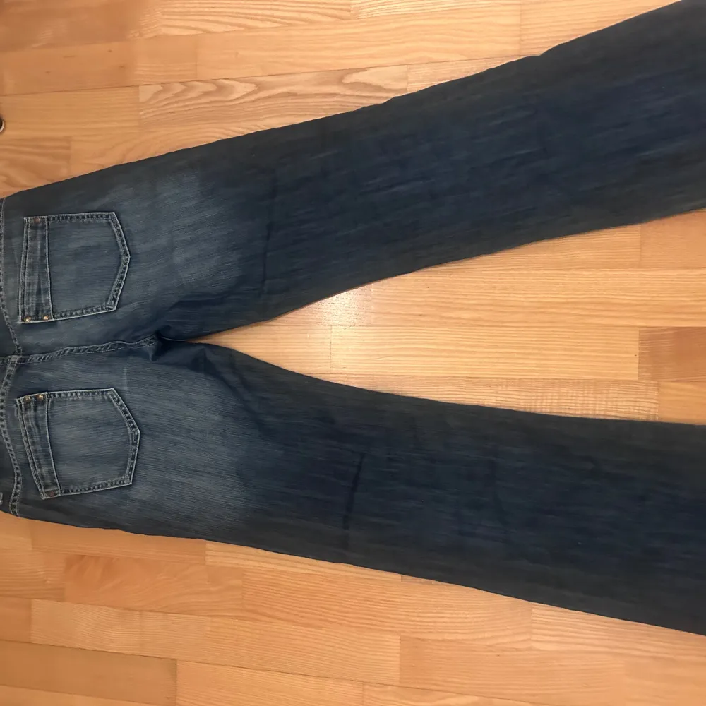Snygga vintage blå bootcut jeans med klassisk femficksdesign. De har en lätt slitning vid fållen som ger en cool, avslappnad look. Perfekta för en casual stil.. Farkut & Housut.