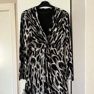 Mönstrad klänning från M.A.P - Snygg klänning från M.A.P med ett svart och grått mönster. Klänningen har en v-ringad design och långa ärmar. 