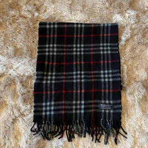  Burberry halsduk Cashmere - Snygg rutig halsduk från Burberry i klassiska färger. Tillverkad av 100% kashmir för en lyxig och mjuk känsla. Perfekt för att hålla dig varm under kyliga dagar. Den har fransar i ändarna som ger en extra touch av stil. Såklart äkta, äkhetscertifikat från Sicuro!