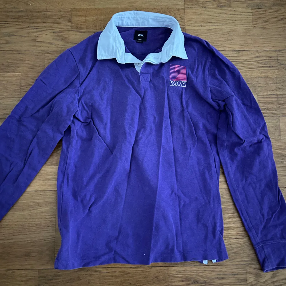 Säljer en snygg lila pikétröja från Vans med vit krage och ett coolt tryck på bröstet. Tröjan har långa ärmar och är perfekt för en avslappnad stil. Bara använt några få tal gånger.. Neuletakit & Villapaidat.