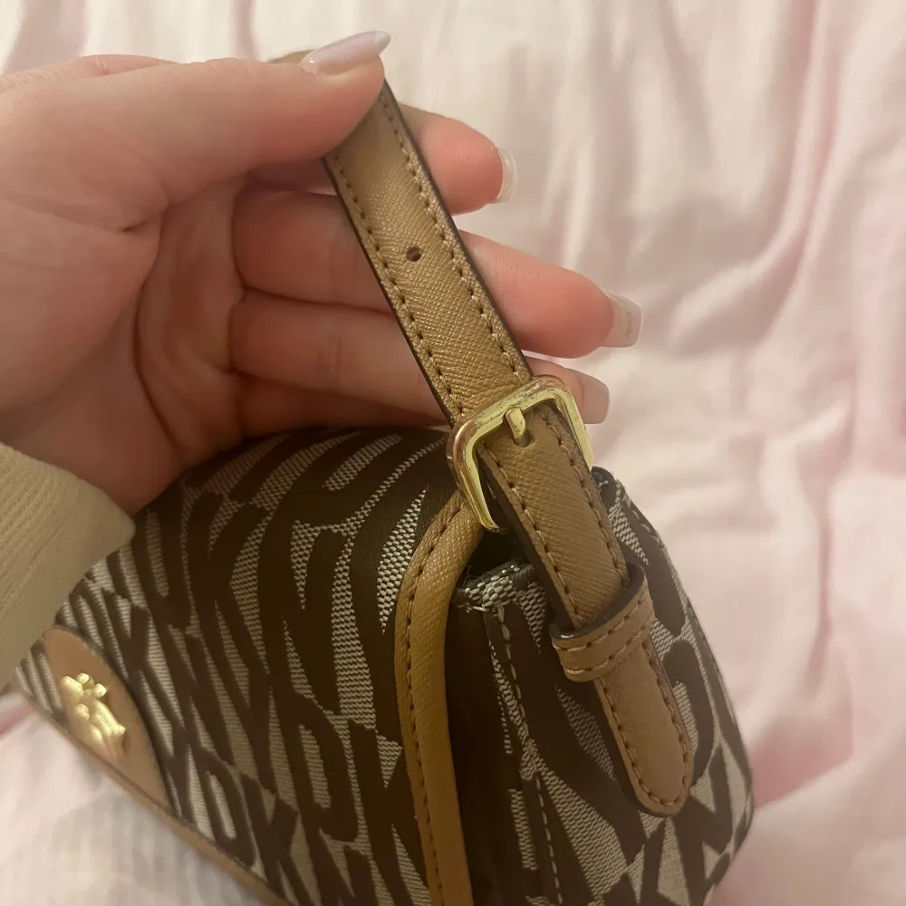 Snygg brun axelväska från DKNY. Väskan har en justerbar axelrem och ett magnetlås. Insidan är rymlig med en dragkedjeficka för extra säkerhet. Små missfärgningar på loggan och guldspännerna. Nypris ca 2300kr. Laukut & Käsilaukut.