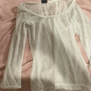 Grön mesh topp från Dolce & Gabbana - Säljer en elegant grön mesh topp från Dolce & Gabbana. Toppen har långa ärmar och en offshoulder-design med volangdetaljer vid halsringningen. Perfekt för att lägga till en touch av lyx till din garderob.