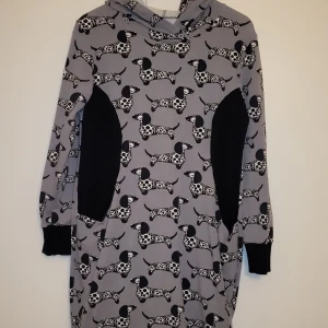 Grå hoodie med taxmönster - Säljer en unik grå hoodie med ett charmigt taxmönster. Tröjan har svarta detaljer vid sidorna och muddar vid ärmsluten. Perfekt för dig som älskar hundar och vill ha en bekväm och stilren look.