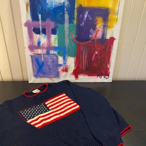 Mörkblå tröja med amerikansk flagga - Snygg mörkblå tröja från Ralph Lauren med en stor amerikansk flagga på framsidan. Tröjan har röda detaljer vid halsringningen och ärmarna. Perfekt för en casual look med en touch av patriotism. Om du undrar något är det bara att fråga på, jag vara så snabbt jag kan🙌🙌