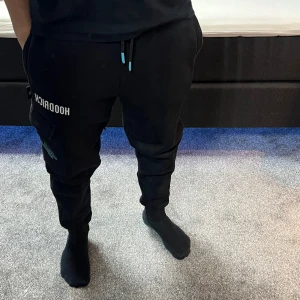 Svarta mjukisbyxor från Hoodrich - Snygga svarta mjukisbyxor från Hoodrich med tryck på benet och praktiska fickor. Byxorna har snörning i midjan och muddar vid bensluten för en bekväm passform. Köpta från JD sports. 