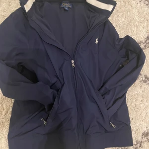 Blå Ralph lauren windbreaker - Snygg blå windbreaker från Polo Ralph Lauren med dragkedja och broderad logga på bröstet. Jackan har långa ärmar och praktiska fickor med dragkedja. Perfekt för en stilren look inför våren och sommaren☀️ Storlek: 14-16, passar XS.