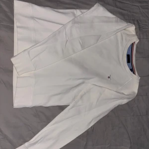 Vit tröja från GANT - Säljer en stilren vit tröja från GANT med rund halsringning och diskret logga på bröstet. Tröjan har långa ärmar och ribbade muddar vid ärmslut och nederkant. Perfekt för en avslappnad och klassisk look.