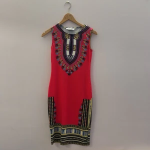 Röd mönstrad klänning från Bacio Azzurro - Snygg röd klänning från Bacio Azzurro med ett färgglatt och detaljerat mönster. Klänningen är ärmlös och har en kroppsnära passform som framhäver figuren. Perfekt för att sticka ut med sin unika design och livfulla färger.