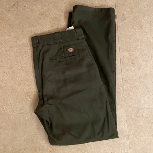 Olivgröna kostymbyxor från Dickies - Snygga olivgröna kostymbyxor från Dickies med en klassisk design. Byxorna har en rak passform och är tillverkade i ett slitstarkt material. Perfekta för en stilren look, säljes då jag inte andvänder dom längre, storlek 32/32