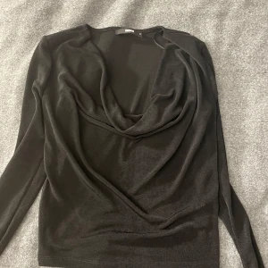 Svart långärmad topp med draperad hals - Snygg svart långärmad topp från bikbok med en elegant draperad hals. Perfekt för en stilren look. Toppen är i ett mjukt och bekvämt material som sitter skönt på kroppen.