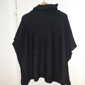 Svart stickad poncho från ONLY - Säljer en stilren svart stickad poncho från ONLY, tillverkad av återvunnen polyester. Perfekt för kyliga dagar med sin bekväma passform och höga krage. Ett mångsidigt plagg som passar till många tillfällen. 🌟