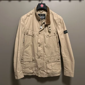 Barbour field jacket - Beige vaxad jacka från Barbour med brunt manchestertyg på kragen. Inga defekter eller liknande. Perfekt nu till våren. Skriv vid funderingar!