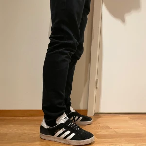Svarta Adidas gazelle - Säljer ett par klassiska svarta Adidas sneakers. Skorna har en vit sula. Perfekta för både fest och vardag🍾. Heeldrag i båda skorna samt allmänt lite sunkiga därav priset. Men sjukt feta.