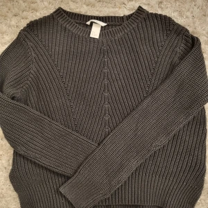 Grå stickad tröja från H&M - Säljer en mysig grå stickad tröja från H&M. Tröjan har en rund halsringning och långa ärmar, perfekt för kyligare dagar. Den har ett snyggt stickat mönster framtill som ger en extra touch. Passar bra till både jeans och kjol.