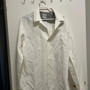 Vit skjorta från Brunello Cucinelli - Säljer en stilren vit skjorta från Brunello Cucinelli i storlek L. Skjortan har en klassisk krage och knappar framtill. Perfekt för en elegant look. Oanvänd i 10/10 skick.