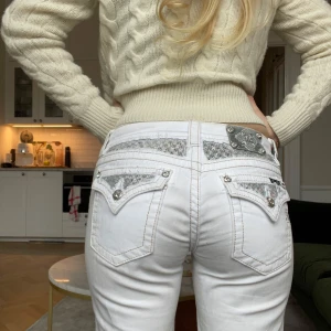 Vita jeans med paljettdetaljer från Miss Me - Snygga vita jeans från Miss Me med glittrande paljettdetaljer på bakfickorna och en dekorativ knapp. Perfekta för att ge din outfit lite extra bling! De har en klassisk femficksdesign och en bekväm passform. Lågmidjade och rak passform. 