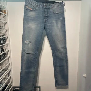 Blå jeans med slitningar - Snygga blå jeans ifrån diesel med slitningar på ena benet. De har en klassisk femficksdesign och en dragkedja med knappstängning. Perfekta för en avslappnad stil. St 32/32