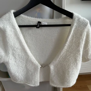 Vit fluffig bolerotopp från HM - Säljer en supermjuk och fluffig vit bolerotopp från HM. Toppen har korta ärmar och en snygg detalj framtill. Perfekt för att lägga till en mysig touch till din outfit. 🐑✨