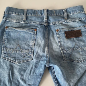 Blå jeans från Wrangler - Snygga blå jeans från Wrangler med klassisk femficksdesign och märkets logga på bakfickan. De har en knappgylf och bälteshällor, perfekt för en avslappnad stil.