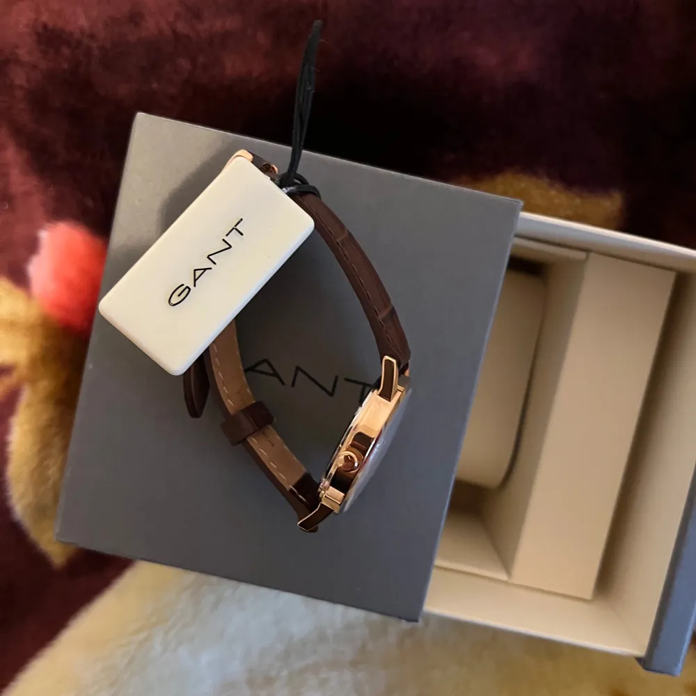 Snygg damklocka från GANT med brun läderrem och vit urtavla. Klockan har en stilren design med guldfärgad boett och tydliga markeringar. Perfekt för den som vill ha en klassisk och tidlös accessoar. Helt ny med plast och allting på! Nypriset är runt 1650kr. . Asusteet.