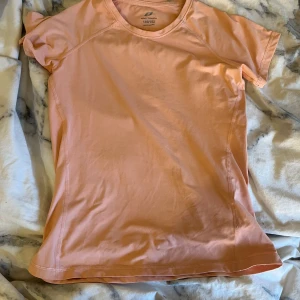Rosa t-shirt från Decathlon - Säljer en rosa tränings  t-shirt i storlek 146/152. Den har korta ärmar och är tillverkad i ett lätt och bekvämt material, perfekt för träning. T-shirten har en enkel design med små dekorativa detaljer på ryggen.