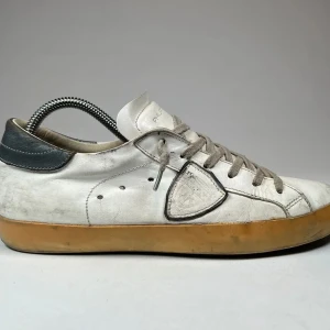 Vita sneakers från Philippe Model - Snygga vita sneakers från Philippe Model med grå snörning och en kontrasterande mörk häl. Skorna har en klassisk design med en gummisula i beige ton. Perfekta för en stilren look.