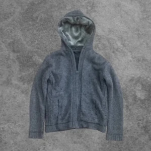 Stickad cardigan med päls - Säljer en mysig grå stickad jacka med huva och mjukt foder. 100% ull. Super bra kvallite! Fur i luvan av högsta kvallite. Italiensk design och sjukt eftertraktad. Storlek M men kan även passa S eller L beroende på.