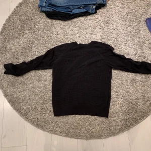 Svart tröja från Calvin Klein - Säljer en stilren svart tröja från Calvin Klein. Tröjan har en ribbad krage och ett diskret mönster på framsidan. Perfekt för en avslappnad men ändå snygg look. 