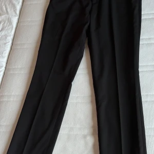 Svarta kostymbyxor - Eleganta svarta kostymbyxor med en klassisk rak passform. Perfekta för en stilren look. Byxorna har diskreta fickor. 