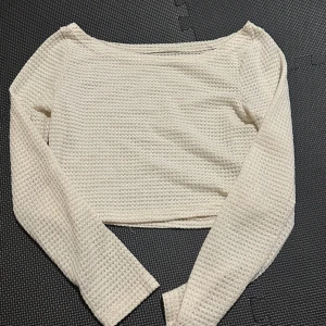 Vit stickad  topp - Säljer en vit stickad  topp med långärmade ärmar. Den har en unik stickad struktur som ger en luftig och stilren look. Perfekt för att lägga till en touch av elegans till din outfit. Passar bra till både jeans och kjol.