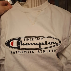 Vit sweatshirt från Champion - Säljer en klassisk vit sweatshirt från Champion med stort broderat märke på framsidan. Tröjan har långa ärmar och en rund halsringning. Perfekt för en avslappnad stil.