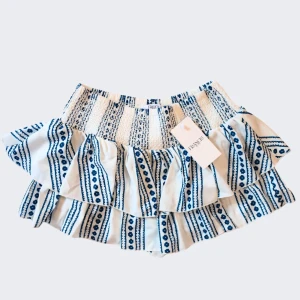 SÖKER KJOL!! - Charmig vit och blå kjol från Joyfolie med volanger och ett vackert randigt mönster. Perfekt för en somrig look med sin korta längd och elastiska midja. Kjolen har en lekfull design som passar utmärkt för varma dagar. Jag söker efter kjolen jag säljer inte den själv