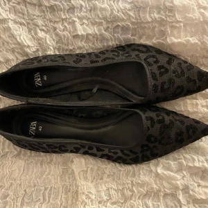 Svarta leopardmönstrade pumps från Zara - Snygga svarta pumps från Zara med leopardmönster och spetsig tå. Perfekta för att ge en elegant touch till din outfit. Klackhöjden ger en stilren look.