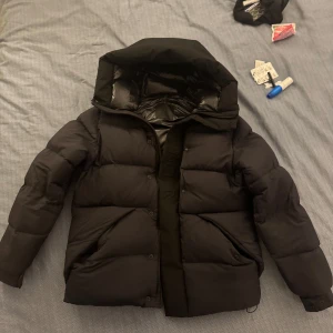 Moncler Madeira | Size 4 - Säljer en svart dunjacka från Moncler som ingen annan i sverige har, med en stilren design. Jackan har en hög krage och en praktisk huva. Den är långärmad och har en diskret Moncler-logga på ärmen. Perfekt för kalla dagar. Storlek 4/XL Men passar Sitter som M jag har S egentligen. Kvitto + Galje finns Ord. Pris 21485