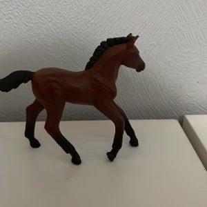 Leksaks häst - Säljer en brun hästfigur i plast med svarta detaljer. Hästen har en elegant pose med lyft ben och en flätad man. Perfekt för samlare eller som leksak.