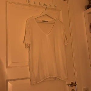 Vit t-shirt från Comma - Säljer en stilren vit t-shirt från Comma med v-ringning. Perfekt för en enkel och klassisk look. T-shirten har korta ärmar och är gjord i ett mjukt material.