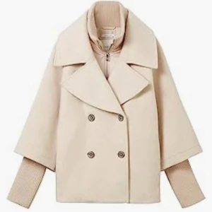 Beige kappa med dubbelknäppning - Snygg beige kappa med bred krage och dubbelknäppning. Jackan har en unik design med trekvartsärmar och ribbade muddar som sticker ut. Perfekt för en stilren look. 