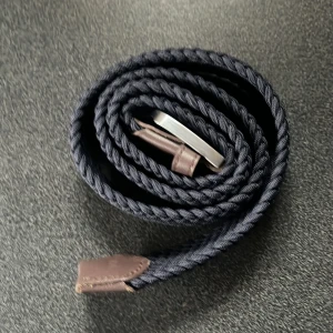 Mörkblått flätat bälte från Onewear - Snyggt mörkblått flätat bälte från Onewear med bruna skinnändar och en silverfärgad spänne. Bältet är helt nytt och aldrig andvänts. Det passar dem flesta eftersom man själv kan justera vilken längd man vill ha, Pris kan diskuteras vid snabb affär
