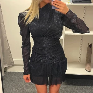 Svart glittrig klänning- maje klänning - Snygg svart glittrig marinblå/svart klänning med långa ärmar och volangdetaljer. Den har en tight passform och en kort längd som ger en elegant look. Perfekt för en kväll ute eller en speciell tillställning. Det är en  Maje liknande klänning, säljer pga av att den ej passar. Detta är bilder från förra ägaren.  Pris går att diskuteras, säljer endast vid bra bud.