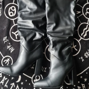 Lårhöga Svarta stövlar med klack - Snygga svarta stövlar i syntetmaterial med hög klack och spetsig tå. De har en stilren design med rynkade detaljer längs skaftet. Perfekta för att ge en elegant touch till din outfit. Bianca ingrosso har liknande. Dom går över knäna. Helt nya och oanvända!