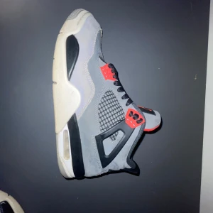 Jordan 4 infread  - Snygga grå och svarta sneakers med röda detaljer och snörning. Skorna har en luftig mesh-design på sidorna och en bekväm sula med synlig dämpning. Perfekta för en stilren look.