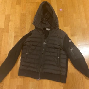 Svart pufferjacka med huva -  en svart cardigan jacka  från Moncler med huva och dragkedja. 