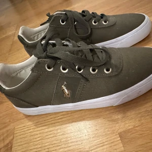 Olivgröna sneakers från Ralph Lauren- Nyskick - Snygga olivgröna sneakers från Ralph Lauren med klassisk design. De har endast använts en gång  vilket endast syns på sulan. nypris var:995kr Har även ett par gråa ute till salu