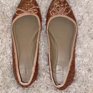 Rosa glittriga ballerinaskor från Esprit  - Snygga glittriga ballerinaskor från Esprit i en fin rosa. Skorna har en söt rosett framtill och är perfekta för att ge en extra touch till din outfit. De är bekväma och lätta att bära hela dagen. Jag har bara haft på den några få gånger och de är i väldigt god skick som man kan se på bilden.