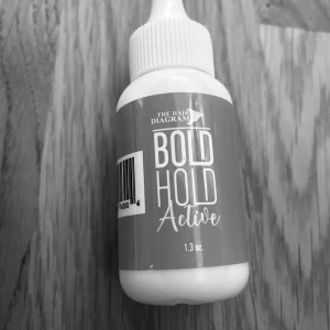 Bold Hold Active från The Hair Diagram - Bold Hold Active är en limprodukt från The Hair Diagram, perfekt för att säkra peruker och hårdelar. Flaskan innehåller 1,3 oz av produkten och har en praktisk applikator för enkel användning. Förpackningen är rosa med vit text och en gul detalj.