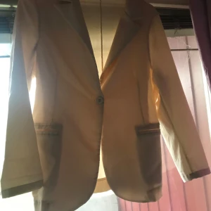 Beige kavaj från Copenhagen Luxe - Säljer en stilren beige kavaj från Copenhagen Luxe. Kavajen har en enkel knäppning framtill och långa ärmar. Perfekt för en elegant look.