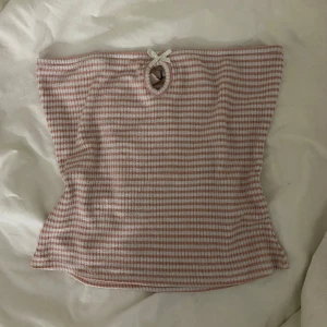 Rosa och vit randig tubtopp - Söt tubtopp i rosa och vit randigt mönster. Toppen har en liten rosett och ett hål framtill som ger en fin detalj. 